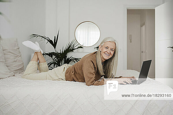 Happy woman lying on bed with laptop at home
