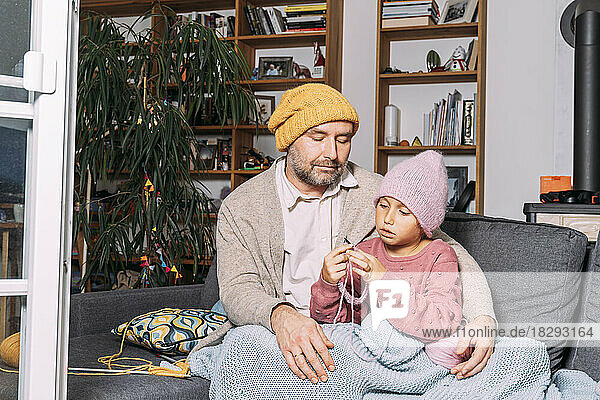 Vater schaut zu  wie seine Tochter zu Hause auf der Couch strickt