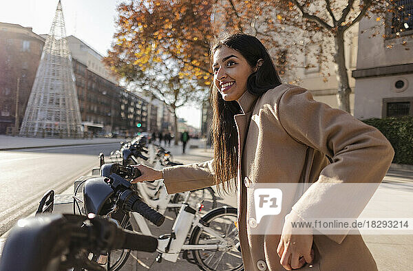 Happy young woman renting bicycle on sunny day