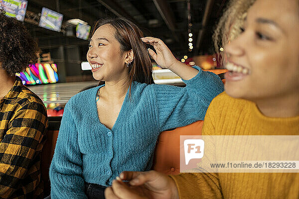Happy young friends sitting on sofa at bowling alley