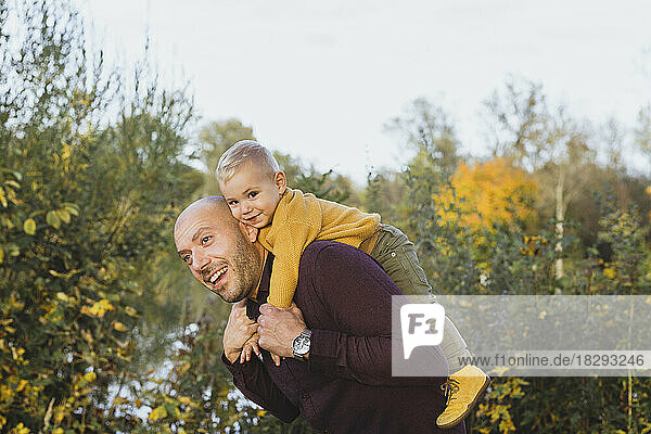 Happy man giving piggyback ride to son in autumn
