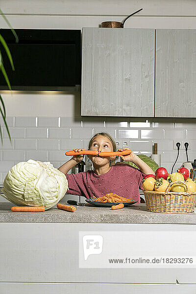 Playful girl having fun with carrots in kitchen at home