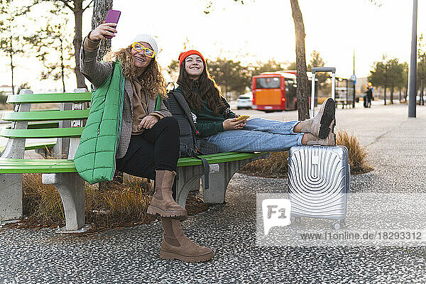 Happy mother with daughter taking selfie though smart phone sitting on bench