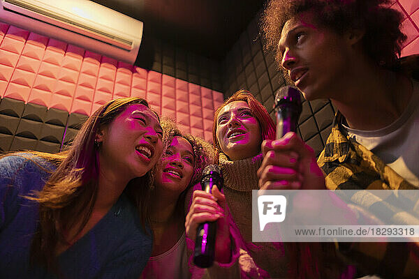 Multiracial friends singing karaoke through microphones at amusement arcade