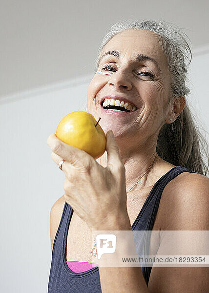 Happy mature woman eating apple at home