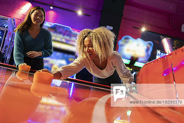 Happy women enjoying playing air hockey at amusement arcade
