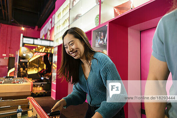Happy young woman playing table soccer at arcade