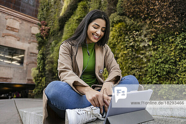 Happy young woman using tablet PC outside vertical garden