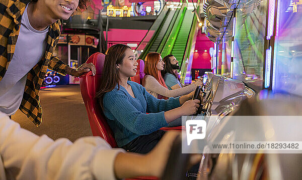 Multiracial friends playing and having fun with driving simulator in amusement arcade