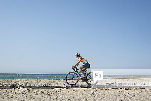 Cyclist riding bicycle at beach in front of blue sky on sunny day