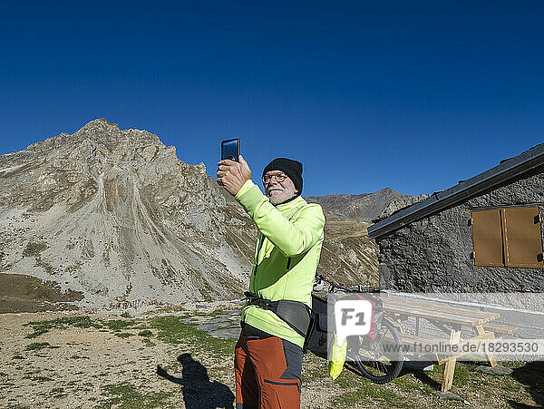 Älterer Mann macht ein Selfie mit dem Mobiltelefon vor einem Berg unter blauem Himmel im Nationalpark Vanoise  Frankreich