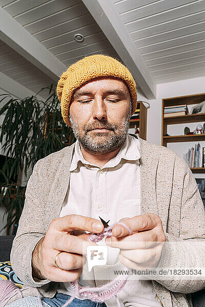 Man in warm clothing knitting on couch at home