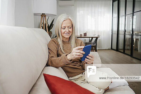 Happy mature woman using smart phone sitting on sofa