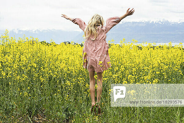 Carefree blond girl with arms raised enjoying in rapeseed field