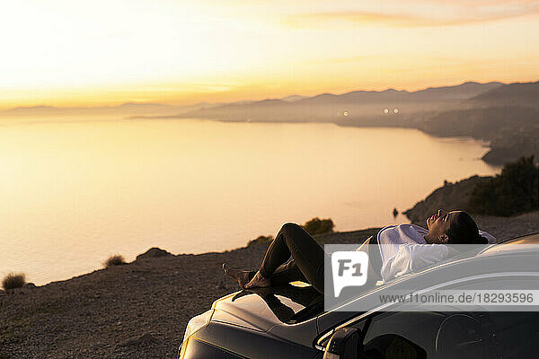 Woman with hands behind head relaxing on hood of car