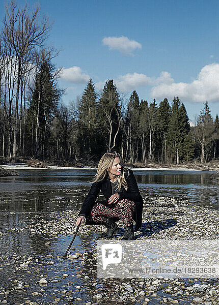Mature woman playing with stick crouching at riverbank