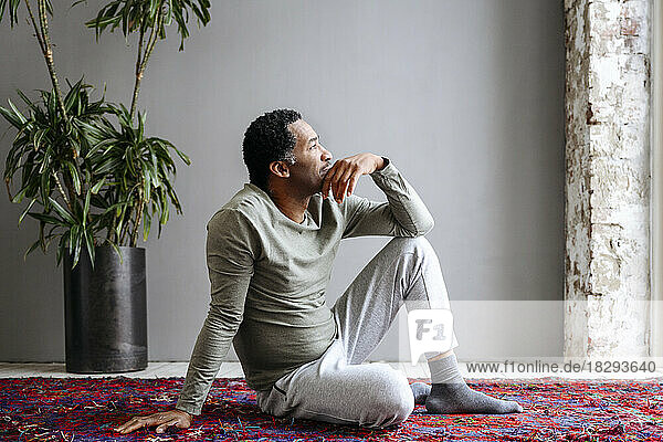 Thoughtful man sitting on carpet at home