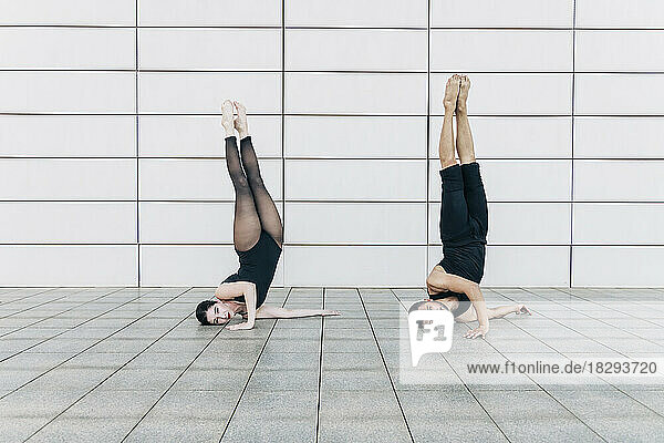 Couple doing headstand together in front of wall