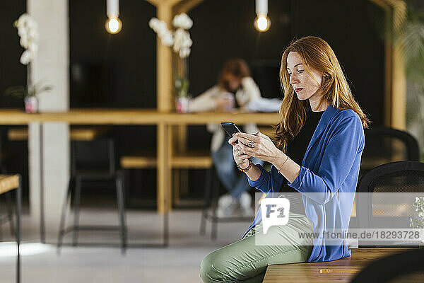 Reife Geschäftsfrau sitzt am Schreibtisch im Büro und nutzt ihr Smartphone