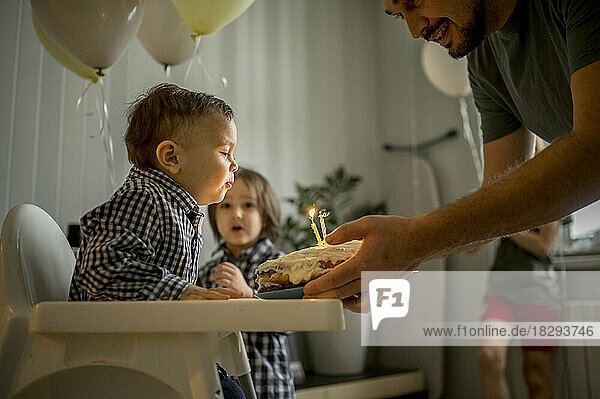 Father with son blowing candles on cake and celebrating birthday with family at home