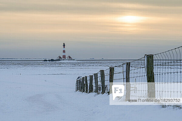 Germany  Schleswig-Holstein  Westerhever  Snow-covered field at sunset with Westerheversand Lighthouse in background