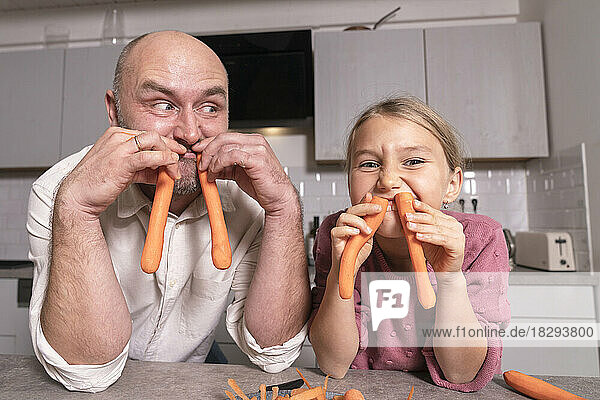 Father and daughter having fun with carrots in kitchen at home