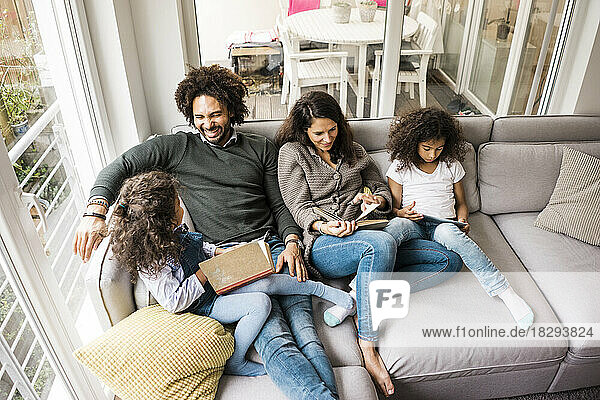 Happy father with mother and daughters reading book on sofa at home