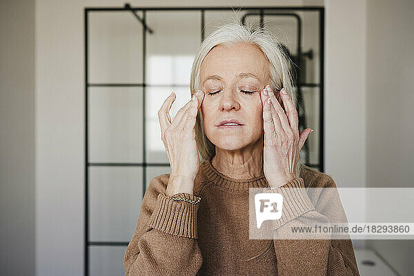 Mature woman applying moisturizer on face at home