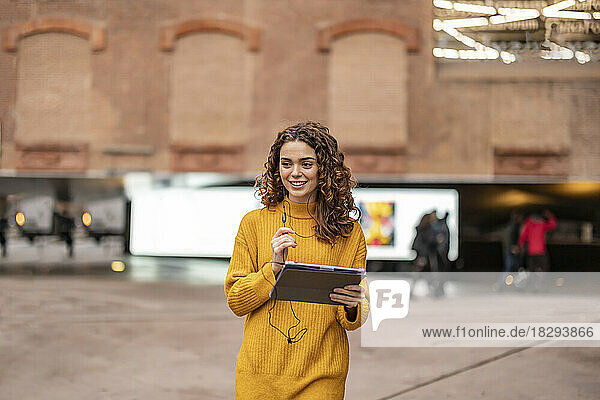 Glückliche junge Frau mit Tablet-PC  die vor dem Gebäude läuft