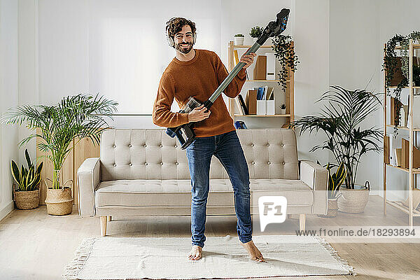 Happy man playing guitar on vacuum cleaner at home