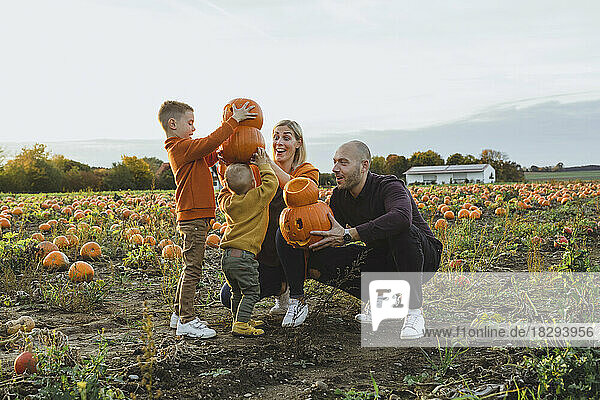 Happy parents with children carrying jack o' lanterns in field