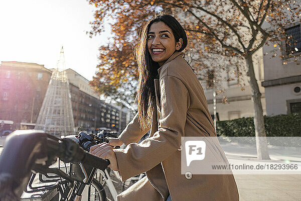 Smiling young woman renting bicycle on sunny day