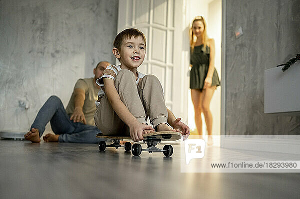 Father playing with son sitting on skateboard and mother standing in background