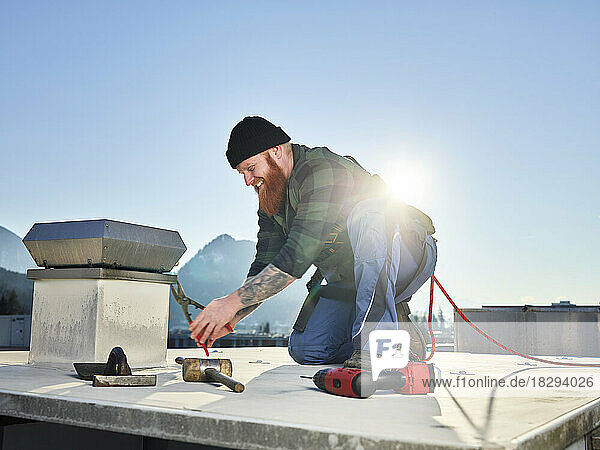Roofer working with pliers at roof on sunny day