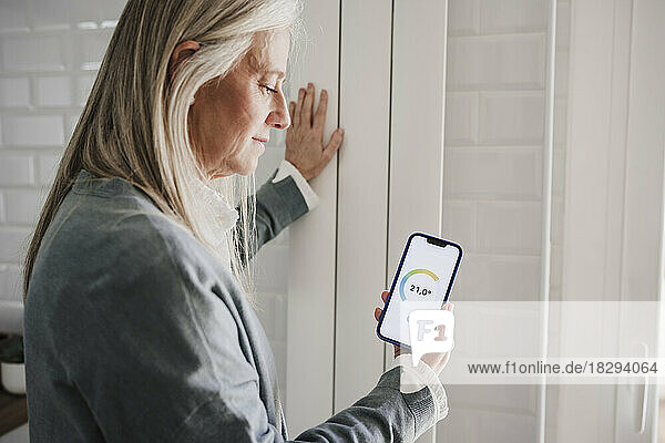 Frau nutzt Hausautomations-App auf Smartphone am Heizkörper