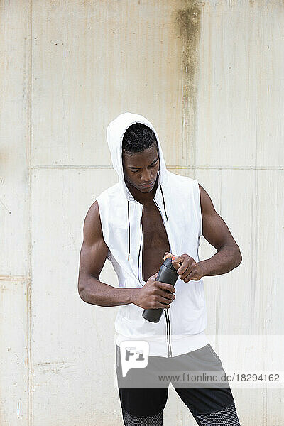 Young man wearing white hooded shirt holding water bottle in front of wall