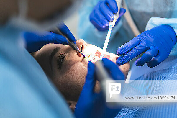 Young dentist with assistant examining patient in clinic