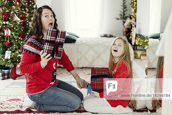 Überraschte Mutter und Tochter mit Geschenken  die zu Hause auf dem Teppich sitzen