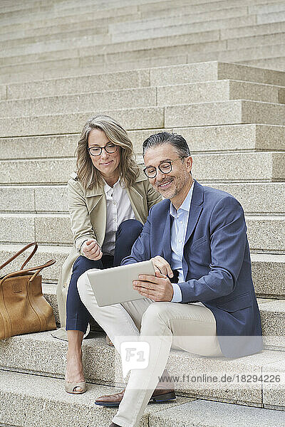 Mature businessman using tablet PC with colleague on steps
