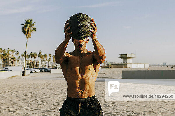 Active athlete with sports ball exercising on beach