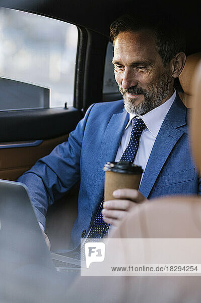 Smiling businessman using laptop sitting in backseat of car
