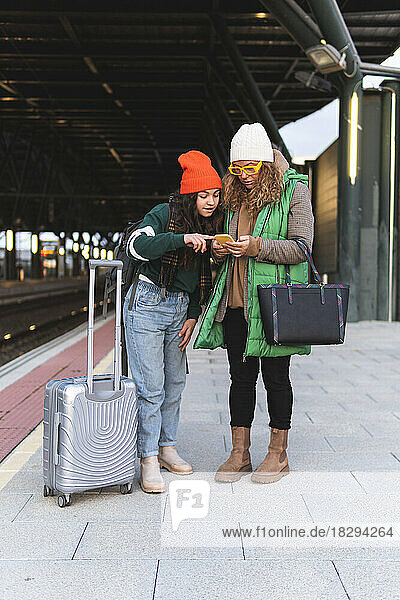 Daughter and mother searching in smart phone at railroad station platform