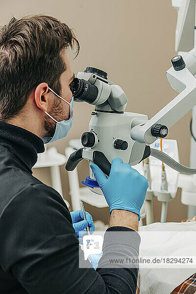 Zahnarzt untersucht die Zähne des Patienten mit dem Mikroskop in der Klinik