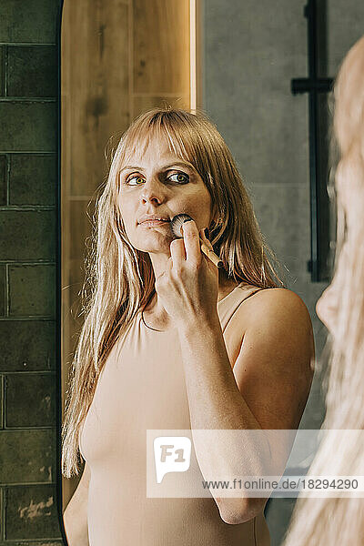 Woman applying make-up with brush in bathroom at home