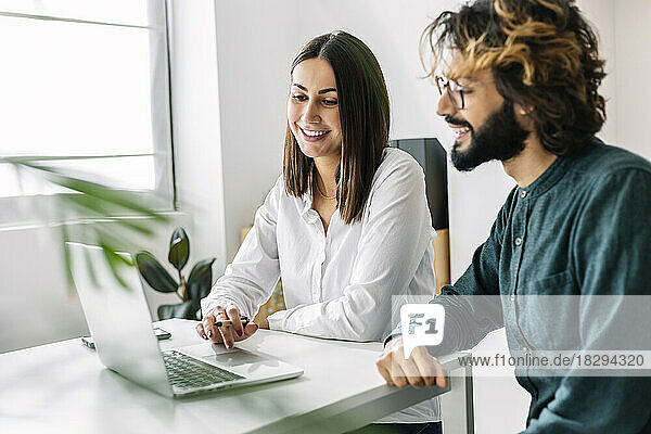 Happy businesswoman using laptop by colleague at desk