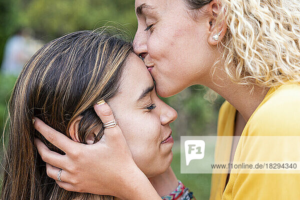 Smiling woman with eyes closed kissing on girlfriend's forehead