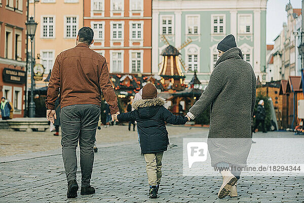Mother and father holding hands with son and walking on footpath at Christmas market