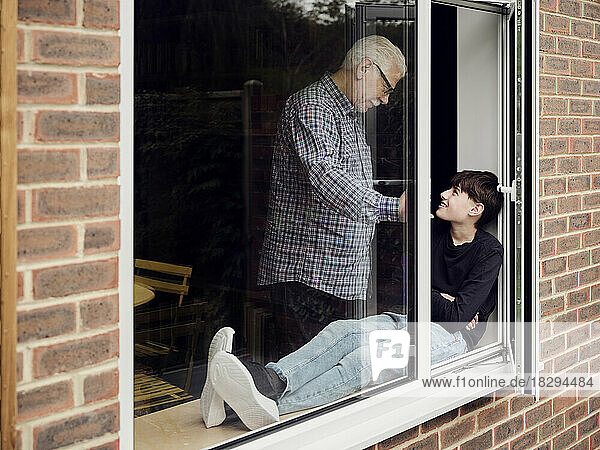 Grandfather and grandson looking at each other by the window at home