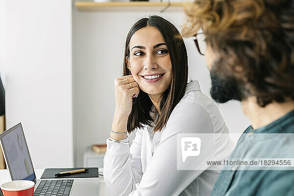 Smiling young businesswoman looking at colleague in workplace