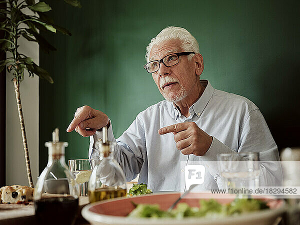 Weißhaariger Mann sitzt gestikulierend am Mittagstisch